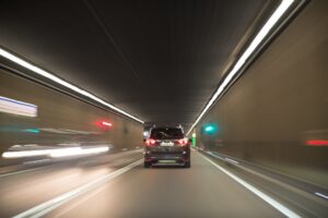 A modern electric vehicle driving through a brightly lit tunnel at high speed, showcasing the seamless integration of EV transportation in urban infrastructure.